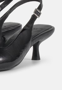 Černé lakované sandály na podpatku s elegantním designem, otevřenou špičkou, křížovými pásky a malým podpatkem. Obsahují detail s obdélníkovou sponou.
