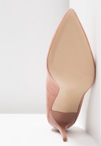 Chaussure à talon stiletto en daim rose à bout pointu reposant sur une surface blanche, semelle orientée vers l'avant montrant la zone de prise texturée et les marques de la marque.