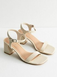 Beige block-heeled sandaler med fyrkantig tå, med ett brett band över foten och en spänne vid ankeln. Strukturerat tygmaterial.