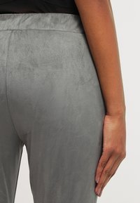 Grijze suède broeken met een gladde textuur, voorzien van een brede elastische tailleband. De stof lijkt zacht en licht glanzend.