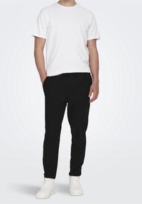 Vit bomulls t-shirt med kort ärm, kombinerad med svarta joggerbyxor med elastisk midja. Avslutad med vita högskurna sneakers.