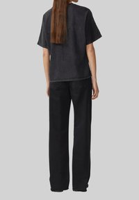 Schwarzes übergroßes Denim-T-Shirt mit kurzen Ärmeln und abgerundetem Saum, kombiniert mit schwarzen lockeren Hosen. Die Rückansicht zeigt einfache Steppnähte.