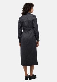 Robe chemise en denim bleu foncé avec des manches longues, taille ceinture et coupe droite. Comprend un empiècement au dos et des fentes sur les côtés à l'ourlet.