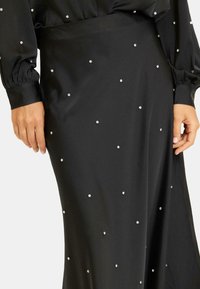 Falda de satén negro adornada con brillantes tachuelas plateadas dispersas, con una textura suave y una silueta ajustada con un ligero drapeado.