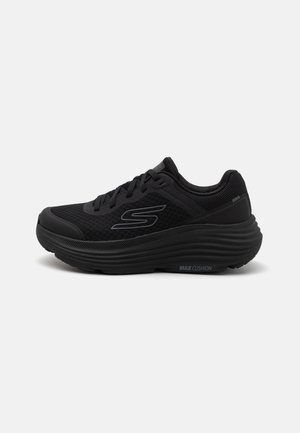Zapatilla deportiva negra con parte superior de malla, suela acolchada y cuello con padding. Presenta un logo en el costado y detalles texturizados en la suela.