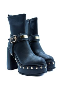 Stivaletti neri con tacco alto realizzati in pelle, dotati di un tacco a blocco, hardware in tonalità oro e dettagli borchiati lungo la piattaforma e la cinghia.