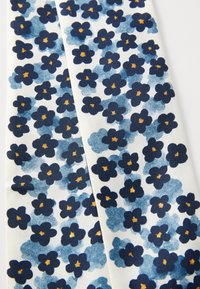 Tissu à motifs présentant de petites fleurs bleues sur un fond blanc, avec des pétales bleu foncé et des cœurs jaunes, caractérisé par un aspect texturé.