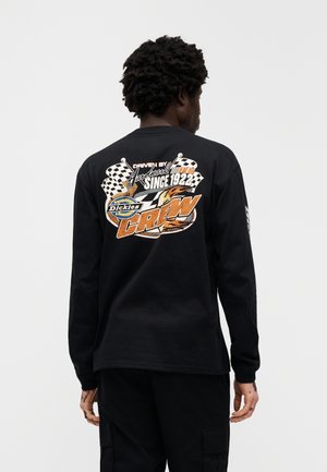 Zwart T-shirt met lange mouwen met een kleurrijke afbeelding op de achterkant met race-motieven, geruite vlaggen en de tekst "Driven by Hardwork Since 1922."