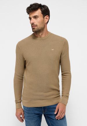 Beige geribde trui met een ronde halslijn, lange mouwen en kleine logo-details op de borst, gemaakt van een zachte gebreide stof.