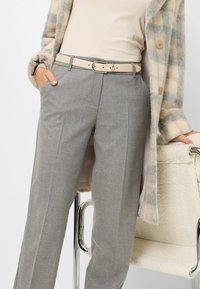 Grijze op maat gemaakte broeken met een rechte snit, voorzien van een lichtbeige riem en zijzakken, gecombineerd met een jas van gemusterde stof.