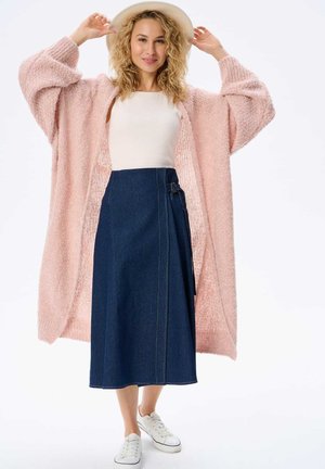 Lichtroze fuzzy cardigan, witte aansluitende top, donkerblauwe spijkerrok met een zijgespelde, en witte sneakers. Het model draagt een hoed met brede rand.