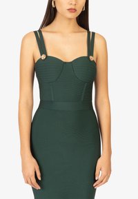 Grünes, figurbetontes Kleid mit einem strukturierten Oberteil und gefalteten Details, dünnen Trägern und floralem Akzenten an den Schultern. Glatte Stoffoberfläche.