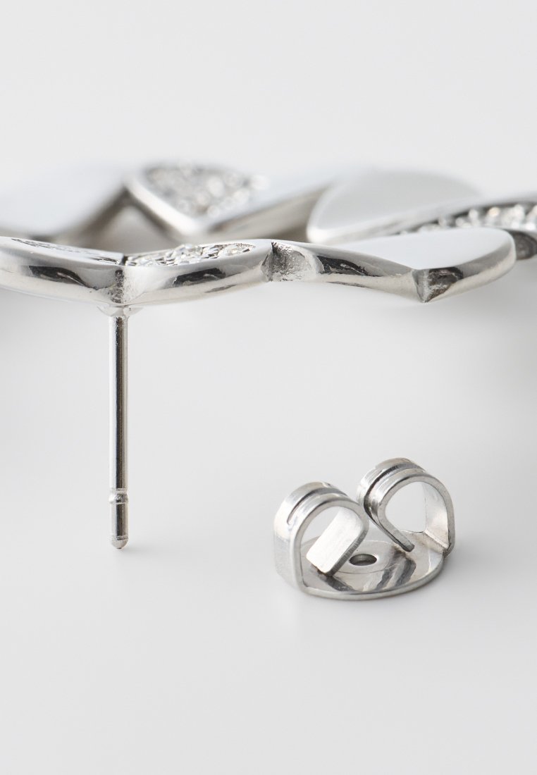 Pendiente de botón en forma de flor plateada con pequeñas piedras claras y respaldo de mariposa separado sobre una superficie blanca.