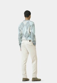 Hellblau und grauer Argyle-Muster-Pullover, cremefarbene Cordhosen und braune Stiefel, von hinten vor einem weißen Hintergrund betrachtet.