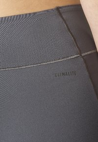 Šedé sportovní legíny Climalite s hladkým povrchem, které mají ploché švy a decentní branding detail poblíž pásu.