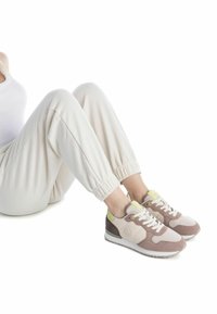 Zapatillas con parte superior de malla y ante en rosa claro, con acentos en gris y amarillo. Suela blanca, diseño de cordones y detalle del logo en el lateral.