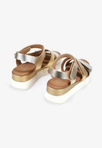 Sandalias metálicas con correas entrecruzadas en tonos plateados y dorados, con una plantilla acolchada y una gruesa suela de plataforma blanca.