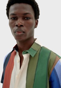 Chemise à manches courtes, multicolore, avec des rayures horizontales en vert, marron, bleu et crème. Dotée d'un col et d'une fermeture à boutons.