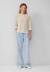 Maglioncino beige chiaro lavorato a maglia, con vestibilità ampia e maniche a tre quarti, abbinato a pantaloni in denim blu chiaro a gamba larga e sneakers bianche.