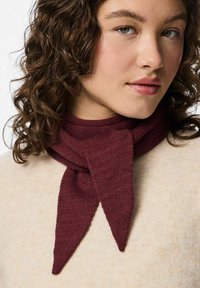 Bordeaux gebreide sjaal met puntige uiteinden, om de nek gewikkeld, met een gestructureerd ontwerp. Draagt over een lichtbeige trui.