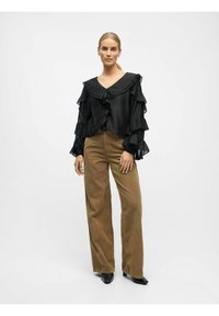 Zwarte, gerimpelde blouse met een V-hals en lange mouwen, gecombineerd met high-waisted, wijde beige corduroy broek en zwarte hoge hakken.