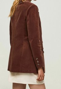 Hnědý kordový blazer se strukturovaným designem, se zdobením knoflíky na manžetách a s rozparkem vzadu pro zvýšenou pohyblivost.