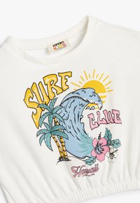 Witte katoenen t-shirt met een kleurrijk surfclubontwerp met een golf, palmbomen, bloemen en zonafbeelding, met een gathered hem-detail.