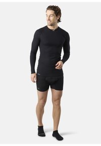 Zwarte geribbelde thermoshirt met lange mouwen gecombineerd met zwarte strakke shorts. Beide kledingstukken hebben een gladde textuur en minimale branding.
