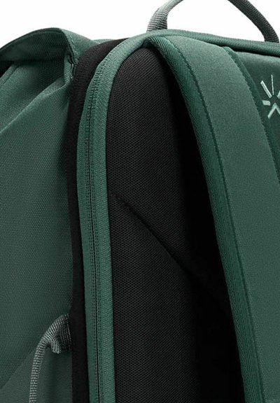 Zaino in tessuto verde con un pannello nero testurizzato, spallacci imbottiti e cuciture rinforzate. Il design enfatizza durata e funzionalità.