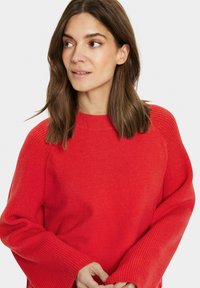 Maglione rosso con scollo rotondo, polsini a costine e una trama morbida, con una vestibilità comoda e maniche scese.