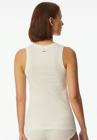 Vit ärmlös tanktopp med ribbat mönster, med rundad halsringning och en liten logotyp på baksidan.