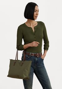 Olivgrön ribbad långärmad topp med henley-krage, kombinerad med blå jeans och en matchande olivfärgad tote-väska med bruna handtag.