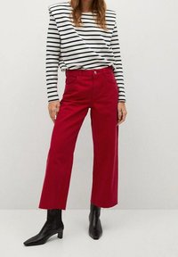 Pantalones anchos rojos con dobladillo deshilachado, combinados con una camiseta de rayas blanca y negra de manga larga. La modelo lleva botines negros.