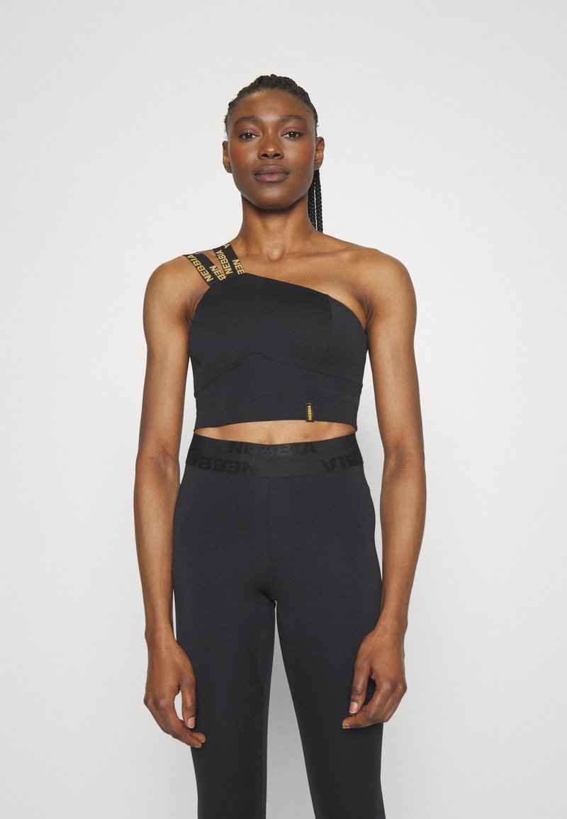 Top corto negro con diseño de un solo hombro; presenta detalles de costura diagonal y una correa con patrón y marca. Combinado con leggings negros de cintura alta.