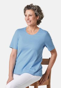 Lichtblauwe t-shirt met korte mouwen van zachte stof met een ronde hals. Draagt met witte broek, tegen een effen witte achtergrond.