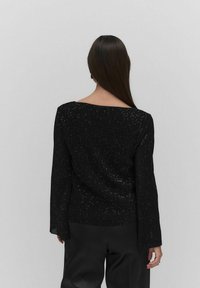 Sort langærmet top med en struktureret, ribbet design, der har subtile glitrende detaljer, firkantet udskæring og slidser i siderne. Glat materiale.