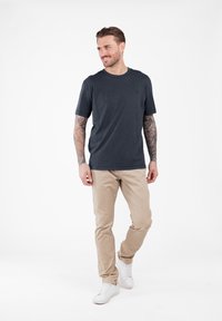 Camiseta gris oscuro de manga corta con cuello redondo, combinada con pantalones slim-fit beiges y zapatillas blancas. Presenta un diseño simple y una tela suave.