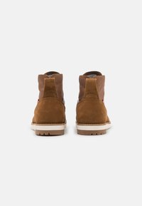 Botas de tobillo de ante marrón con parte superior de cuero color cuero, suela de goma blanca y panel texturizado en contraste en la parte trasera. Sin marcas visibles.