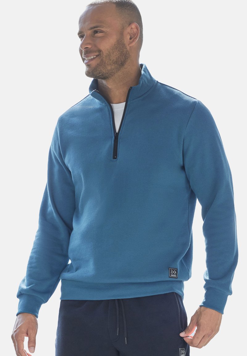 Blue zip-neck sweatshirt with long sleeves, made from soft fabric. Features a black zipper and logo detail at the lower left hem.