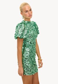 Vestido verde de lentejuelas con mangas cortas abullonadas y silueta ajustada, resaltado por una textura brillante y reflectante.