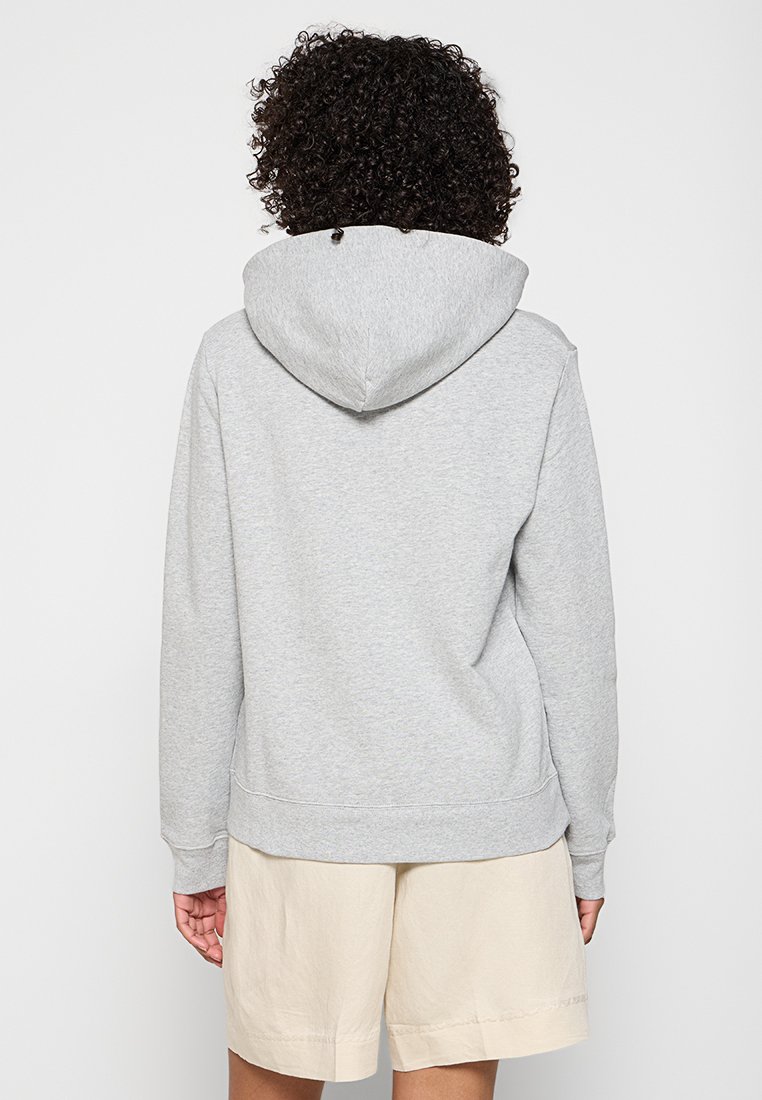 Grauer Kapuzenpullover mit einer geräumigen Kapuze, weichem Material und gerippten Bündchen, kombiniert mit hellbeigen Shorts, von hinten gesehen.