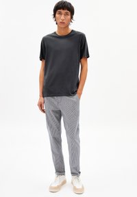 Black short-sleeve t-shirt paired with striped, lightweight pants and white sneakers. Simple, casual design with a relaxed fit and subtle texture.