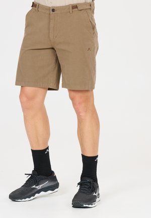 Man draagt beige knielange shorts, zwarte sportsokken en zwarte hardloopschoenen, staand tegen een witte achtergrond.