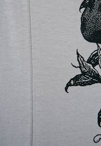 Szary materiał o gładkiej fakturze z czarną grafiką przedstawiającą różę i liście w pobliżu prawej krawędzi.