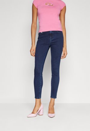 Fitted pink short-sleeve top with a cutout detail, paired with dark blue skinny jeans and light pink patent leather block-heel shoes.