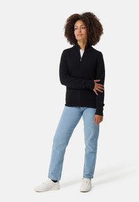 Mustat vetoketjulliset neuletakit, joissa on pitkät hihat ja pehmeä kangas. Yhdistetty vaaleansinisiin farkkuihin ja valkoisiin tennareihin, joissa on yksinkertainen muotoilu.