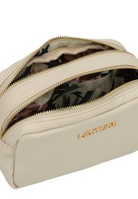 Borsa cosmetica beige con due cerniere dorate, parzialmente aperta per rivelare un rivestimento in tessuto floreale e il logo dorato "LATITUDE" sul fronte.