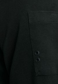 Schwarzes Baumwollhemd mit einer aufgesetzten Tasche, zwei Knopfakzenten und sichtbaren Nahtdetails. Weiche Textur und einfaches Design.