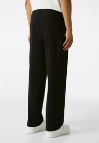 Black wide-leg trousers with a textured finish, elastic waistband, and a single back pocket. Paired with white sneakers.