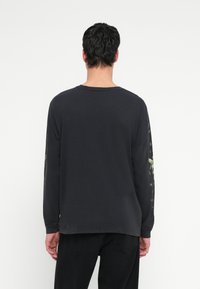 Czarna koszula z długim rękawem i okrągłym dekoltem, zdobiona kolorowymi grafikami na rękawach. Wykonana z miękkiej bawełny o luźnym kroju.